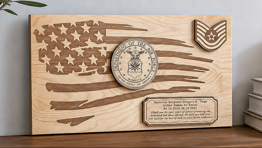 A personalized wooden plaque featuring an engraved American flag design, a circular military emblem, a rank insignia, and a custom nameplate, styled on a shelf next to a potted plant and books.