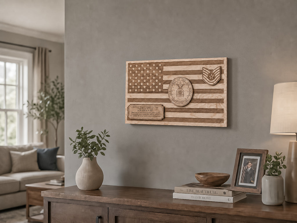 A rectangular wooden wall plaque featuring an engraved American flag design with a military-style insignia and plaque, mounted on a gray wall above a wooden console table in a living room setting.