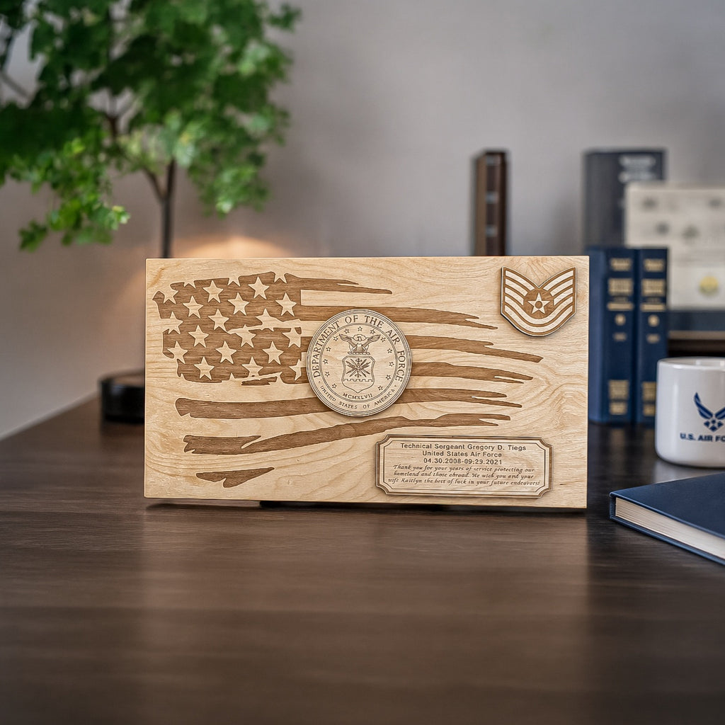 A rectangular wooden keepsake plaque with an engraved American flag design, a circular military-style emblem, and a small U.S. Air Force Seal